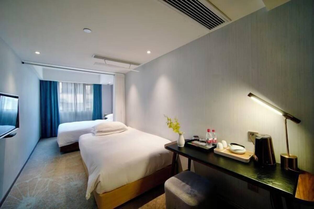 A hotel room with two beds, a desk with a lamp, a TV, and a window with curtains.