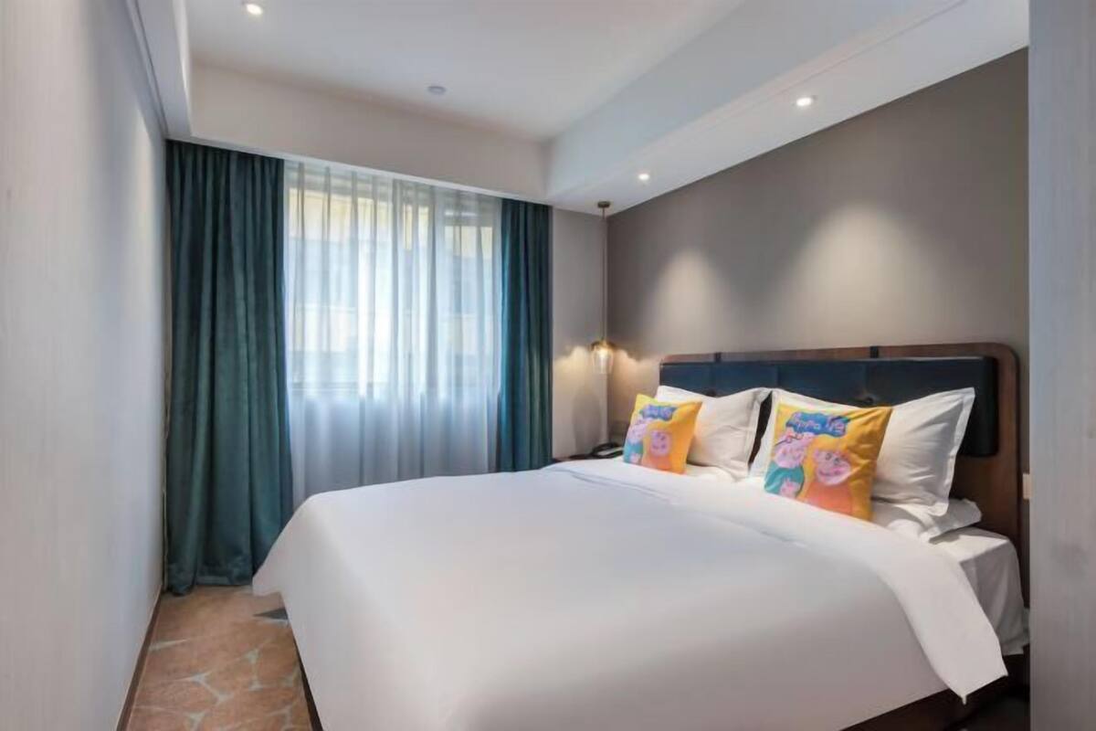 A hotel room with a large bed, a nightstand, a lamp, and a window with curtains.