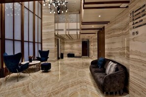 Un hall d’entrée spacieux avec un sol en marbre, un canapé en cuir foncé, des fauteuils bleus et un lustre.