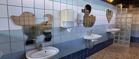 A restroom with three sinks, each with a mirror above. There are soap dispensers and a hand dryer on the wall. The floor has a patterned tile design.