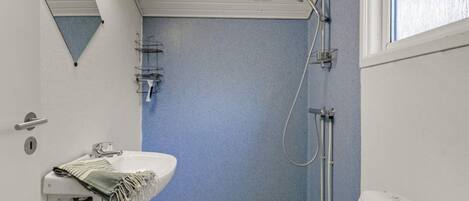 A small bathroom with a blue shower wall, a white sink, and a window.
