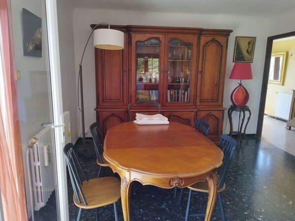 A dining area with a wooden table and chairs, a cabinet with glass doors, a floor lamp, and a radiator. - Villa with swimming pool in the hills above Lodève (Lodève)