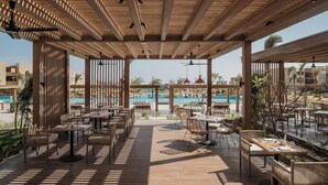 Een terras buiten met houten pergola's, tafels en stoelen, met uitzicht op een zwembad.