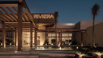 Un edificio moderno con un llamativo letrero 'RIVIERA', una piscina y un área exterior bien iluminada con plantas.