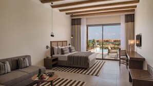 A hotel room with a bed, a sofa, a desk, a TV, a balcony with a pool view, and a ceiling with exposed beams.
