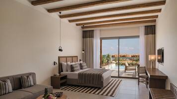 Une chambre d’hôtel comprenant un lit, un canapé, un bureau, une télévision, un balcon avec vue sur la piscine et un plafond avec des poutres apparentes.