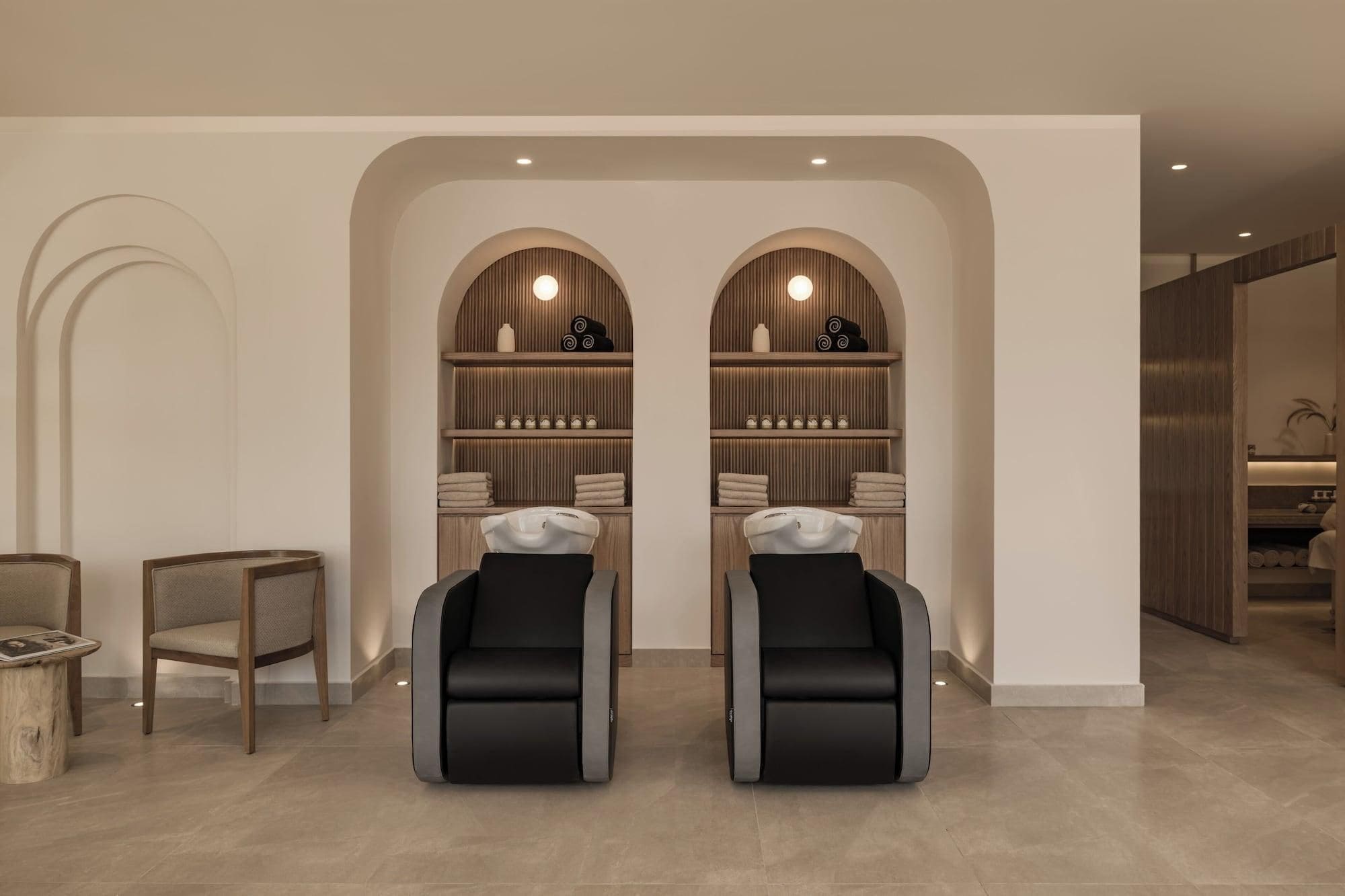 A spa room with two massage chairs, wooden shelves with towels, and a small wooden table.