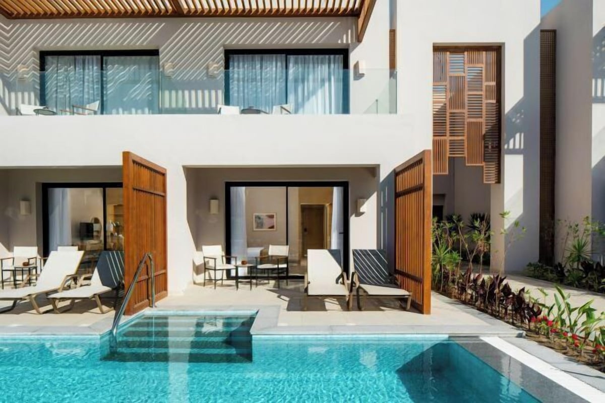 A modern hotel with a pool, lounge chairs, and a well-maintained garden.