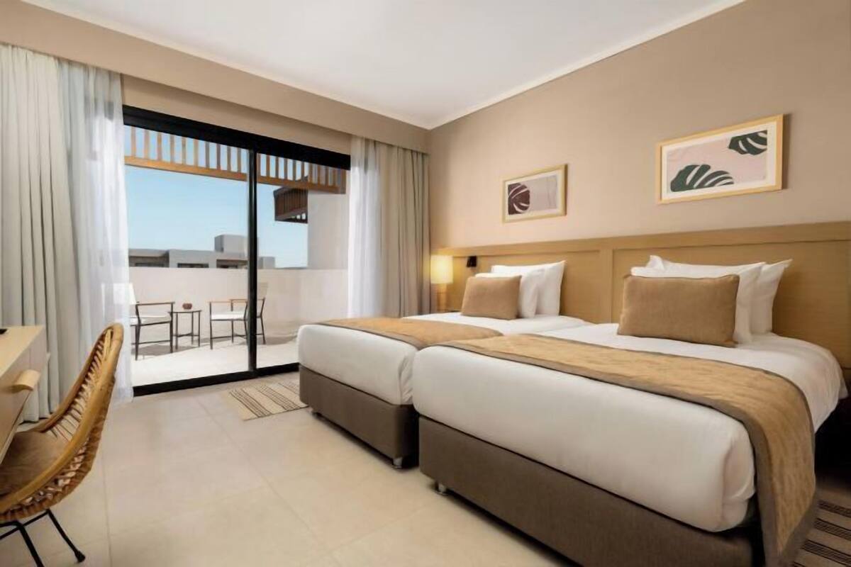 A hotel room with a large bed, a desk, a chair, and a balcony with a view.