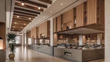 A modern hotel lobby with a central reception desk, wooden paneling on the walls, and a large potted plant.