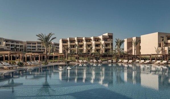 A pool with lounge chairs and palm trees, surrounded by multi-story buildings.
