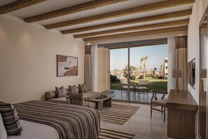 A hotel room with a bed, a sofa, a dining table, and a TV. There is a large window with a view of palm trees and a pool.