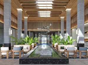 A lobby with a central water feature, seating areas, and a modern ceiling design. - JAZ Elite Riviera (Marsa Alam)
