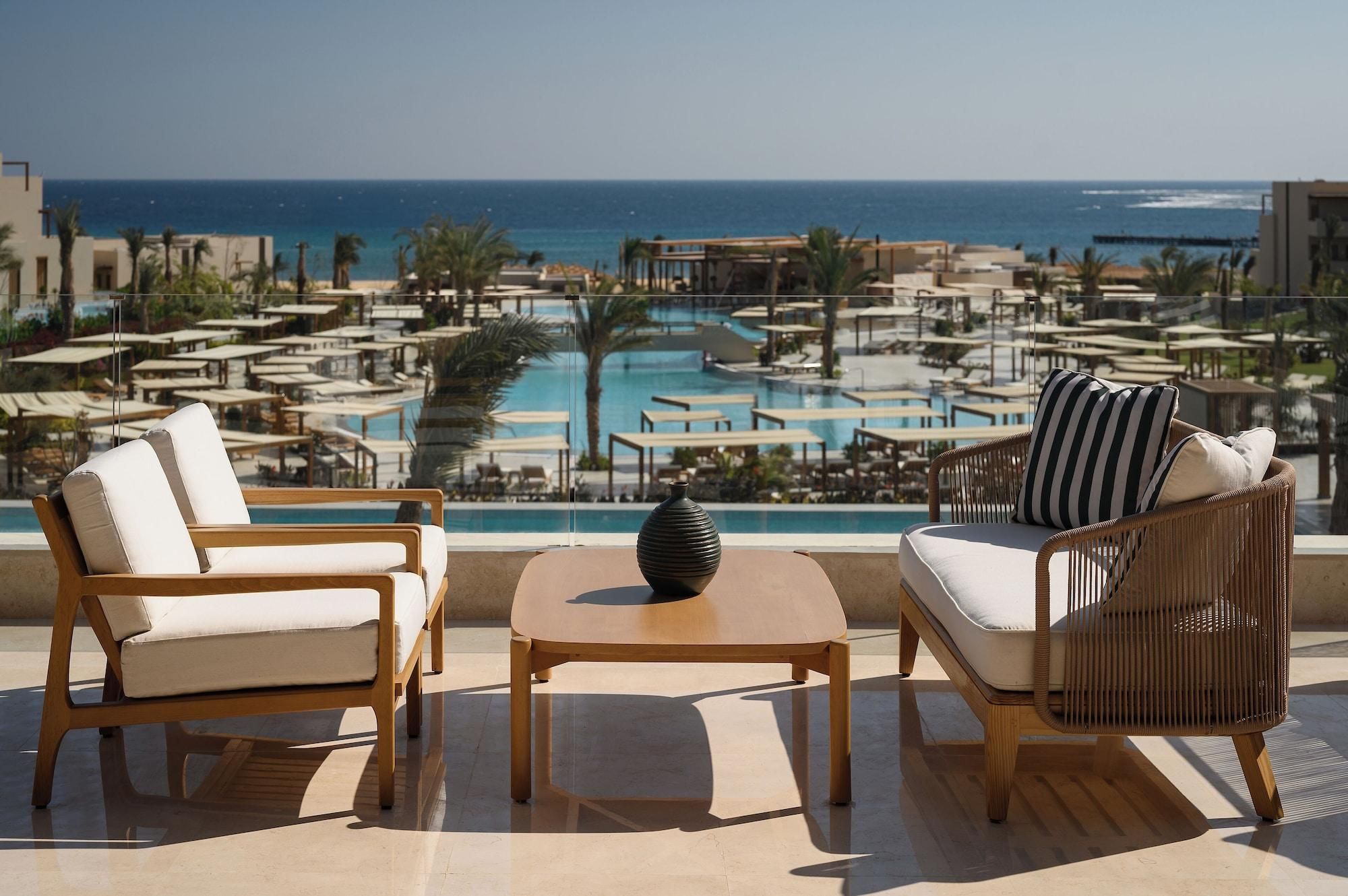 A terrace with two lounge chairs, a small table, and a view of a pool and beach.