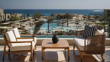 A terrace with two lounge chairs, a small table, and a view of a pool and beach.