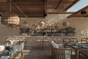 An outdoor bar area with wooden furniture, hanging wicker lamps, and a stone wall backdrop. - JAZ Elite Riviera (Marsa Alam)