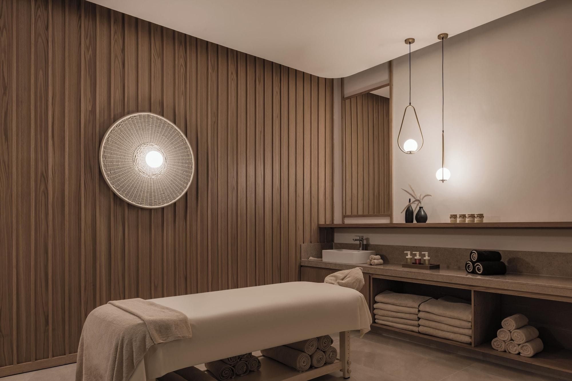 A modern spa room with a wooden wall, a round light fixture, a bench, and a vanity with towels.