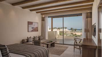 Ein Hotelzimmer mit Bett, Sofa, Couchtisch, Fernseher und einem Balkon mit Blick auf den Strand.