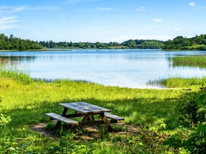 A picnic table by a calm lake with a forested shoreline. - 4 Person Holiday Home in Hampen (Hampen)