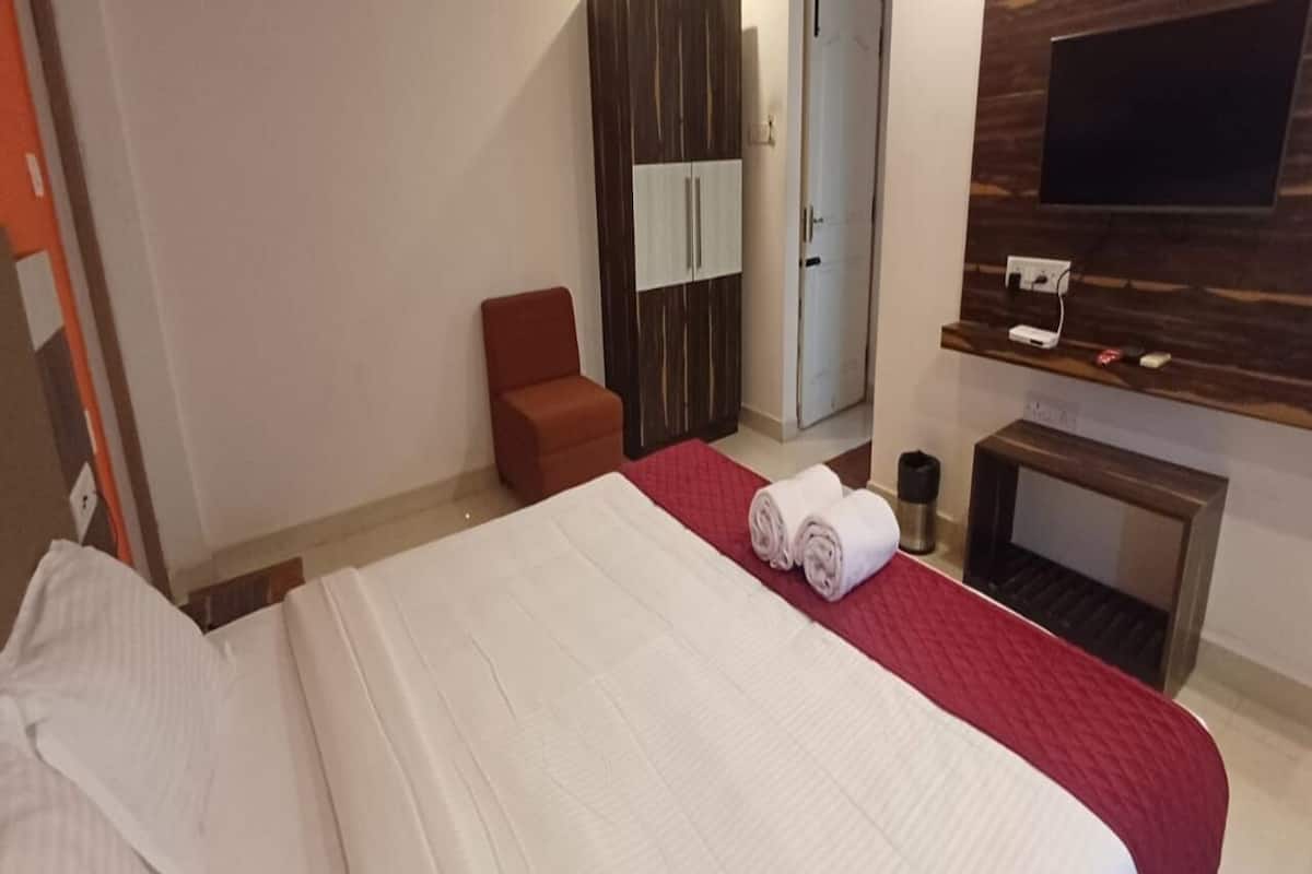 A hotel room with a bed, a red chair, a wardrobe, and a TV mounted on the wall.