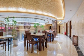 Een hotel lobby met een ronde kroonluchter, potplanten en een gepolijste marmeren vloer.