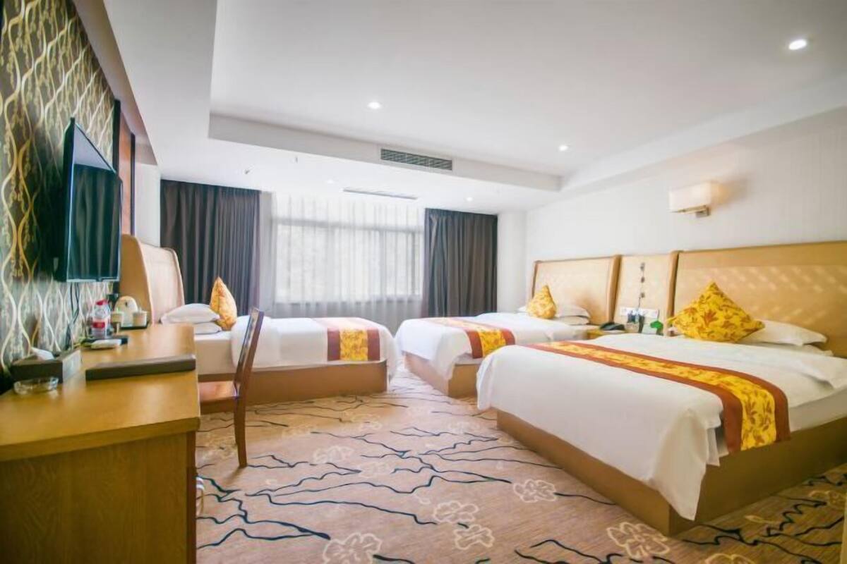 A hotel room with two beds, a desk, a TV, and a window with curtains.
