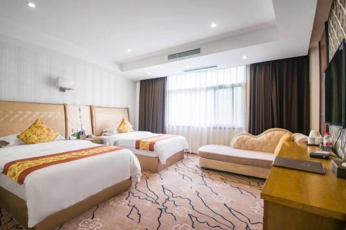 A hotel room with two beds, a sofa, a desk, and a large window with curtains.
