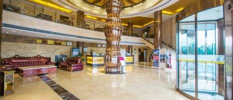 A spacious lobby with a central column, a reception desk, and a staircase leading to upper floors.