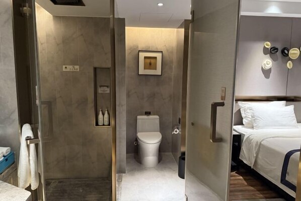 Une salle de bain moderne avec une douche à l’italienne, des toilettes et un lit avec du linge de lit blanc.