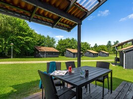 Un espacio de estar al aire libre techado, con una mesa y sillas, rodeado de edificios bajos con techos de metal.