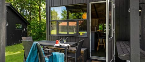 Une terrasse extérieure couverte, avec une table et des chaises, une terrasse en bois et une vue sur un quartier résidentiel.