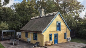 Ett gult hus med ett halmtak, en träveranda och en liten veranda med utemöbler.