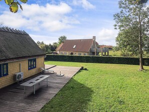A house with a thatched roof and a brick extension, a wooden deck, and a well-maintained lawn.