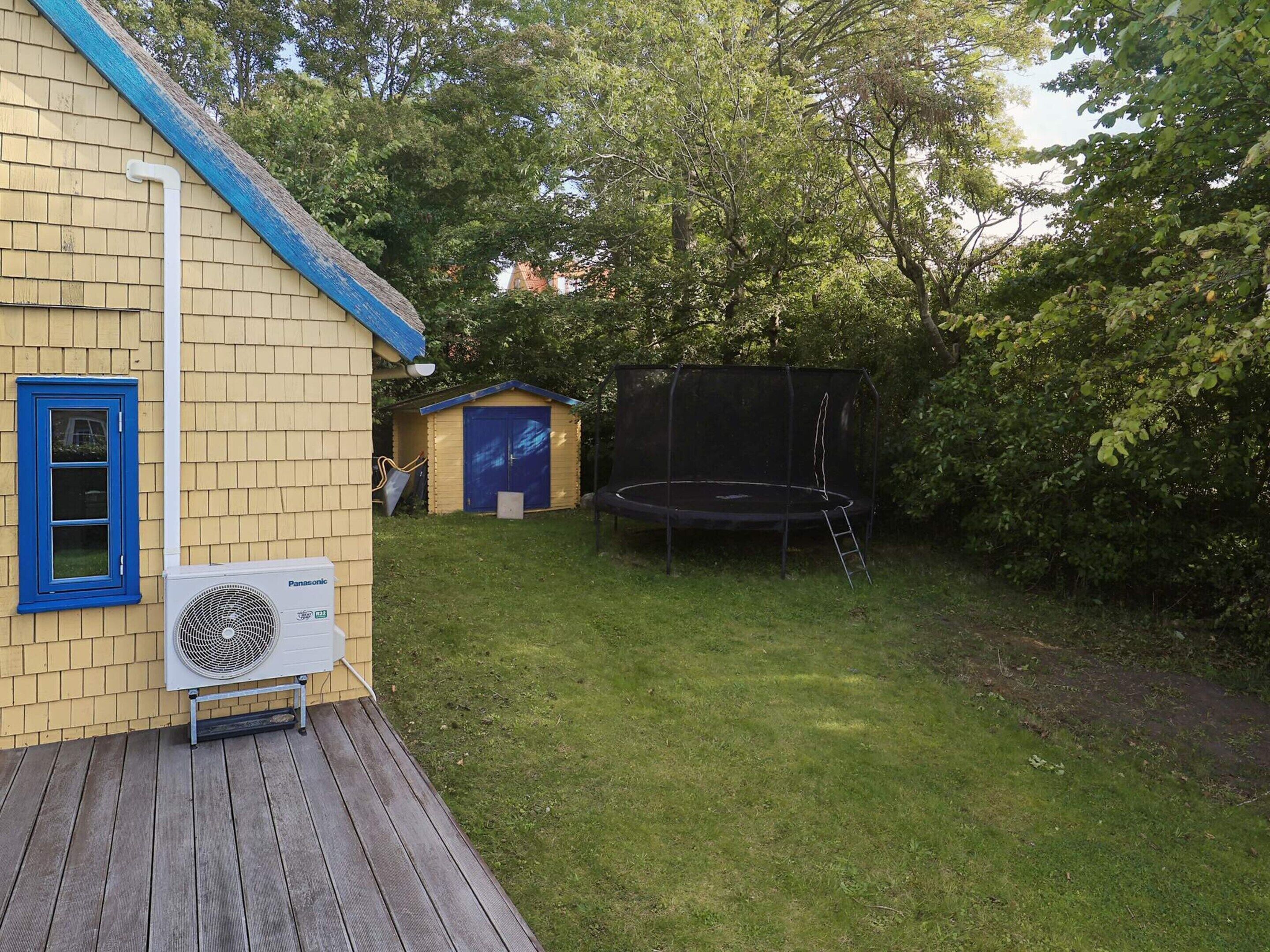 A house with a wooden deck, a blue-framed window, a small shed, a trampoline, and a garden.