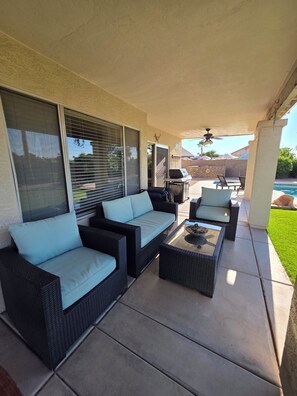 An outdoor patio with wicker furniture, a grill, and a pool.