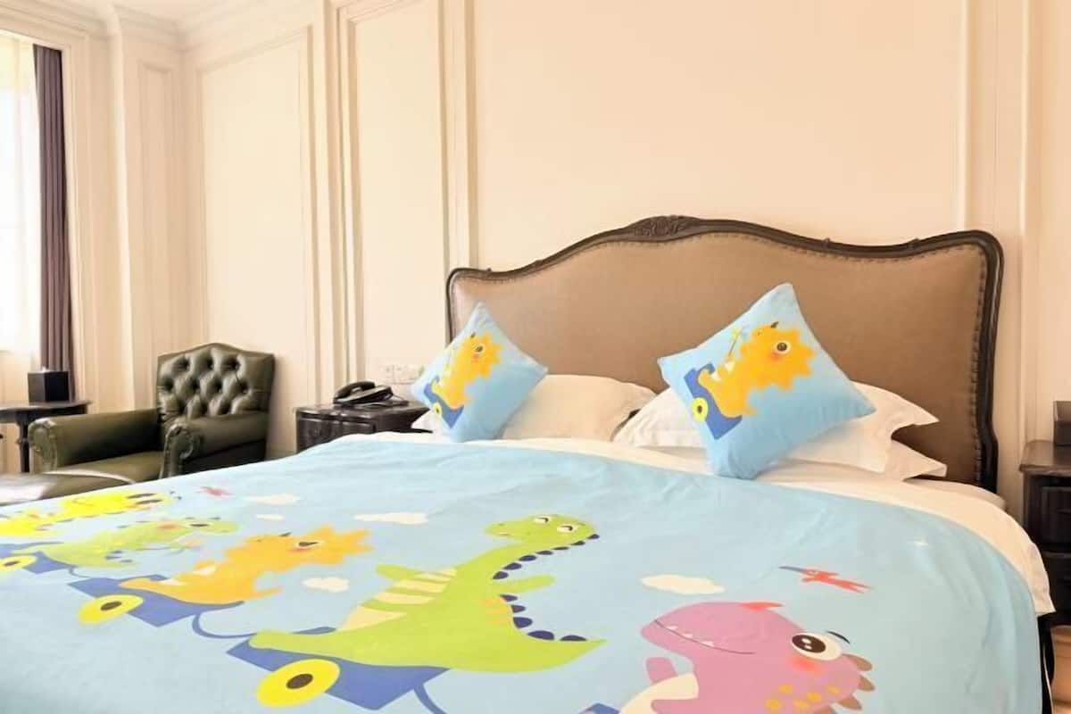 Una camera d'albergo con un letto, una poltrona verde, un comodino e una finestra con tende.