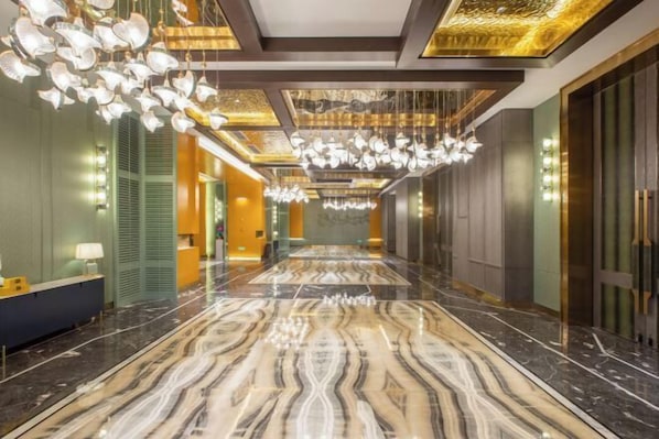 Un vestíbulo de hotel con piso de mármol, candelabros modernos y un mostrador de recepción.