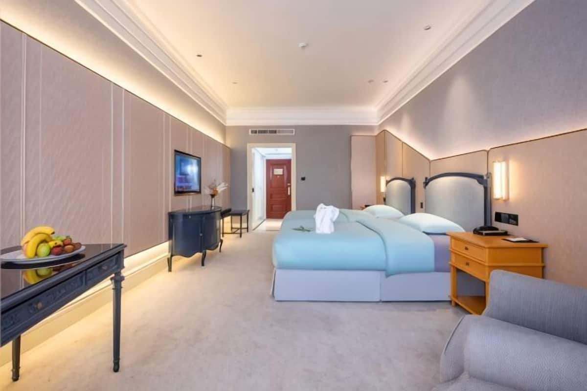 Camera d'albergo con un letto, comodino, lampada e un tavolino con frutta.