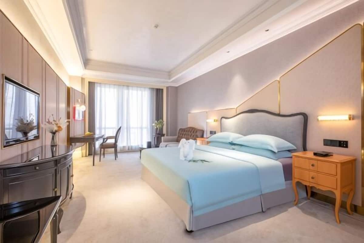 Una camera d'albergo con un letto, comodino, scrivania, sedia e un'ampia finestra.