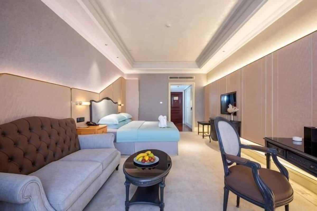 Una camera d'albergo con un letto, un divano, un tavolino con frutta, una televisione e una scrivania con una sedia.