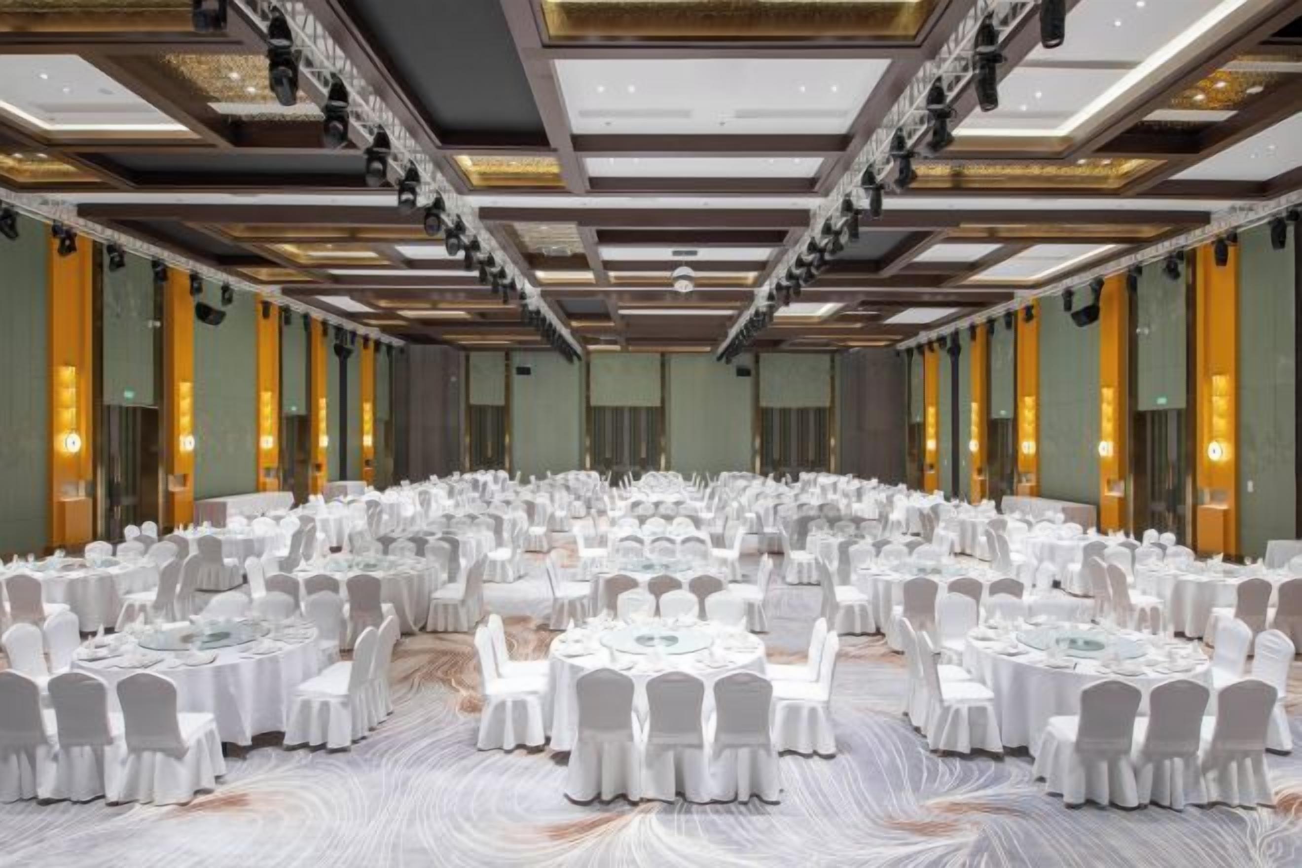 A large banquet hall with round tables and chairs, high ceilings, and modern lighting.