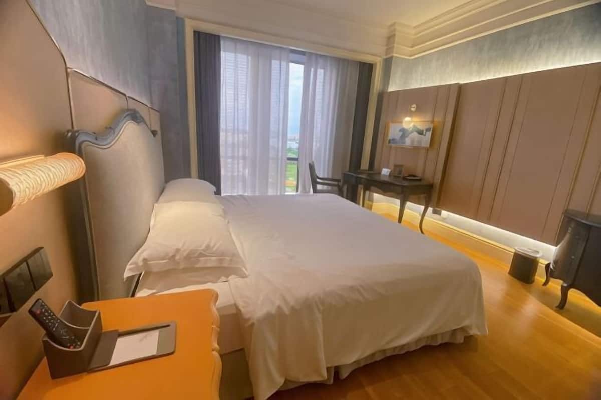 Una camera d'albergo con un letto, una scrivania con una lampada, una sedia e vista sull'esterno.