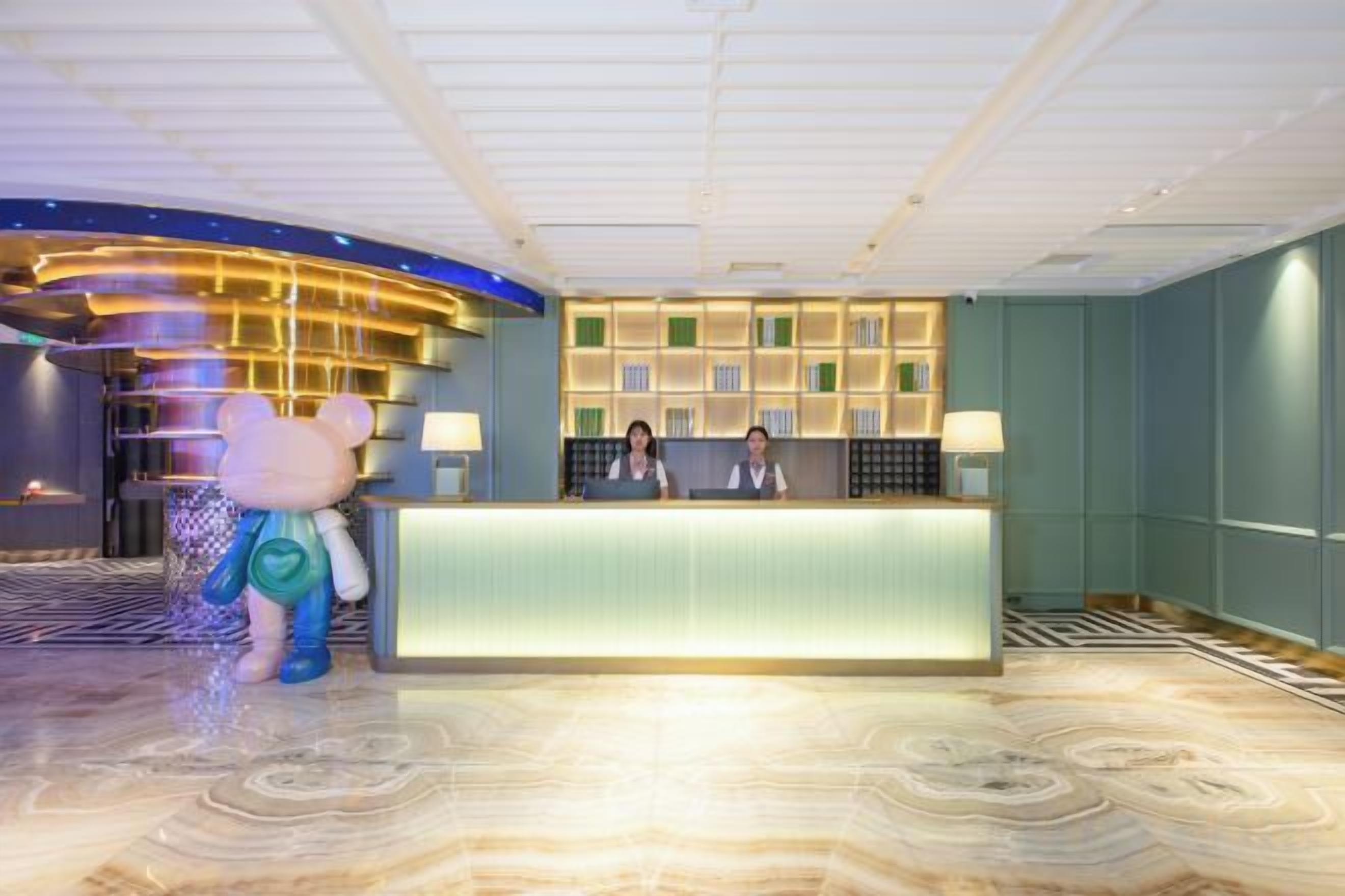 A hotel reception area with a reception desk, two receptionists, and a large bear statue.