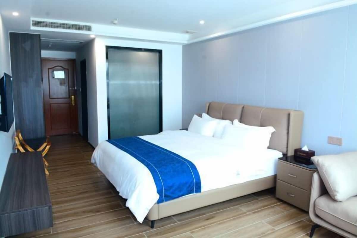 Ein modernes Hotelzimmer mit Bett, Schreibtisch, Stuhl, Fernseher und einer Schiebetür.