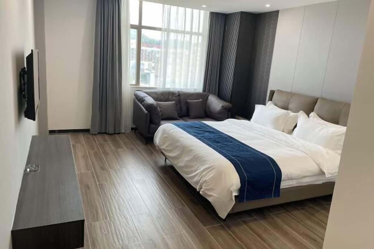 Ein modernes Hotelzimmer mit Bett, Sofa, Fernseher und großem Fenster mit Vorhängen.
