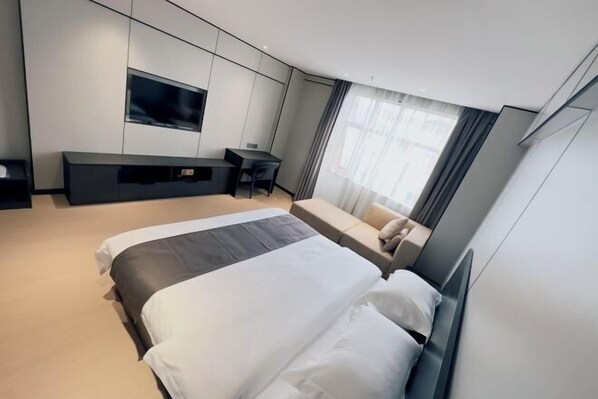 Quarto de hotel moderno com uma cama grande, escrivaninha, televisão de tela plana e um sofá.