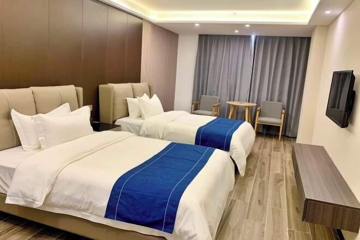 Ein Hotelzimmer mit zwei Betten, einem kleinen Tisch, zwei Stühlen, einem Fernseher und einem Vorhang.