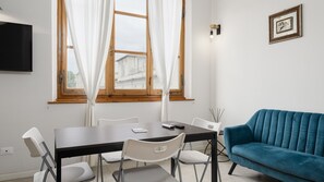 Ein modernes Wohnzimmer mit einem dunklen Holztisch, weißen Stühlen, einem blauen Sofa und einem Fenster mit weißen Vorhängen.