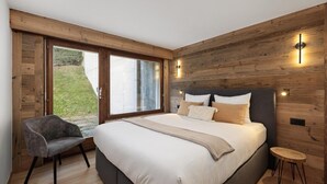 A bedroom with a large bed, a chair, a small stool, and a wooden wall.