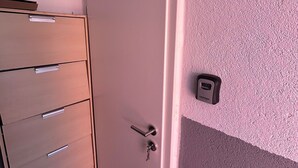 Una habitación con puerta cerrada, un armario de madera con varios cajones y un dispositivo de seguridad fijado a la pared.